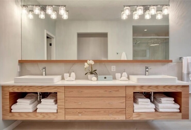 Meuble de salle de bains double vasque en bois clair avec tiroirs et rangements ouverts, avec grand miroir mural et éclairage LED.
